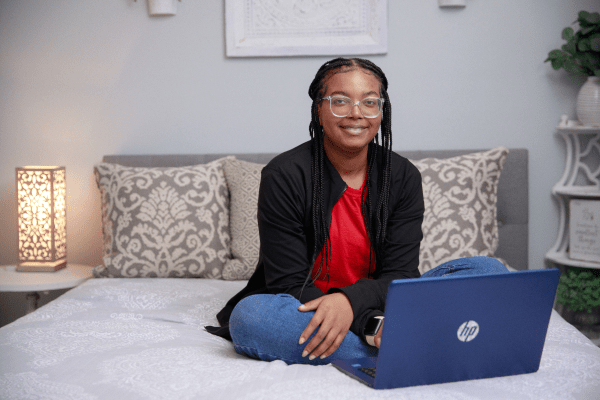 Student seated on bed with her laptop.